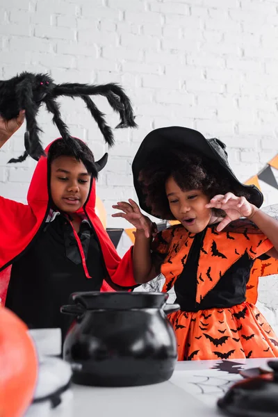 Niños afroamericanos en trajes de halloween preparando poción en caldero de bruja - foto de stock