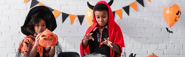 African american kids in halloween costumes preparing potion in witch cauldron, banner — Stock Photo