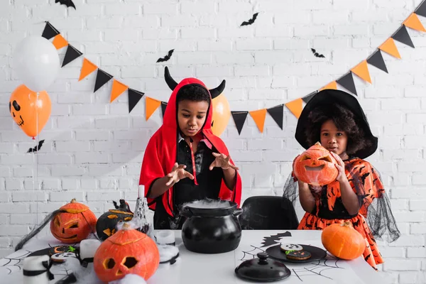 African american children in halloween costumes preparing potion in witch cauldron — Stock Photo