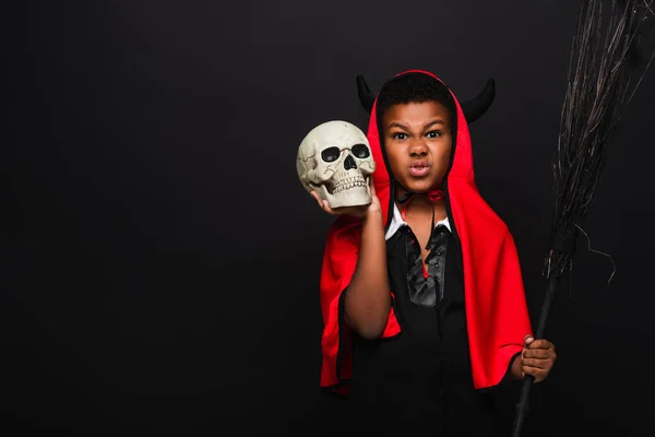 Scary african american boy holding broom and skull isolated on black — Stock Photo