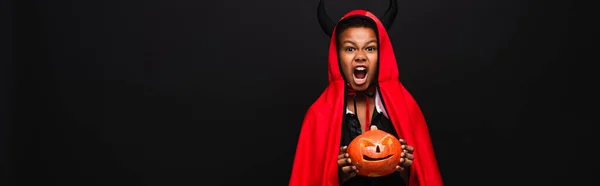 Scary african american kid holding carved pumpkin isolated on black, banner — Stock Photo