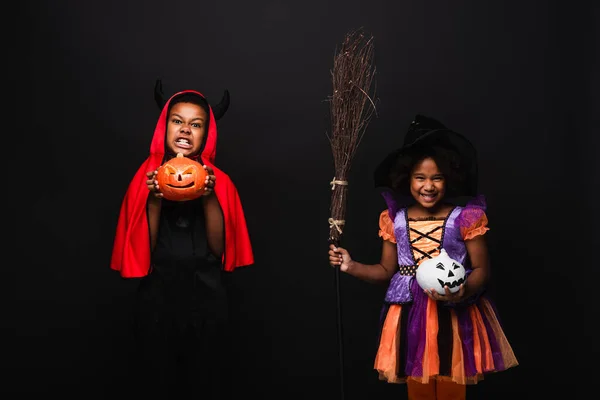 Crianças africanas americanas em trajes de Halloween segurando abóboras esculpidas isoladas em preto — Fotografia de Stock