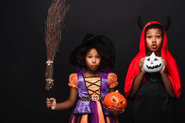 Enfants afro-américains effrayants en costumes d'Halloween tenant citrouilles isolées sur noir — Photo de stock