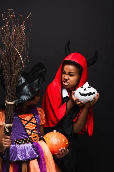 Африканские американские дети в костюмах на Хэллоуин держат жуткие тыквы изолированные на черном — стоковое фото