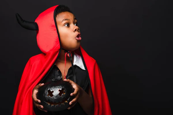 Spooky african american kid holding carved dark pumpkin isolated on black — Stock Photo