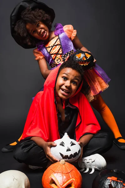 Crianças africanas americanas em trajes de Halloween segurando abóboras esculpidas em preto — Fotografia de Stock