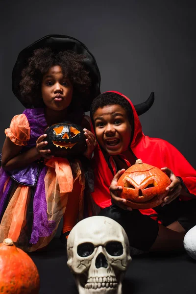 Afro-americanos irmãos em trajes segurando assustador halloween abóboras no preto — Fotografia de Stock