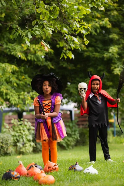 African american kids in halloween costumes holding brooms on backyard — Stock Photo