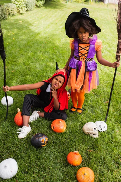 High angle view of african american children in halloween costumes holding brooms outside — Stock Photo