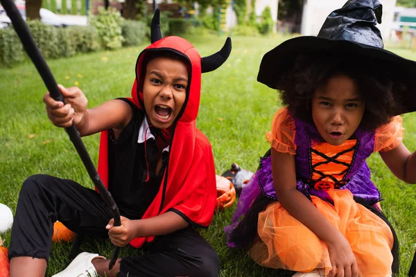 Hermanos afroamericanos en disfraces de Halloween gritando mientras juegan en el patio trasero - foto de stock