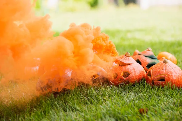 Orange smoke near carved pumpkins on green lawn — Stock Photo