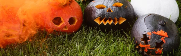 Orange smoke near carved and spooky pumpkins on green lawn, banner — Stock Photo