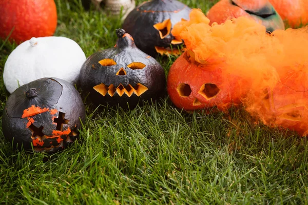 Orange smoke near carved and spooky pumpkins on green lawn — Stock Photo