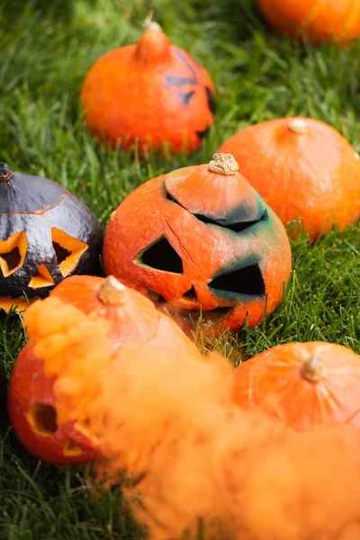 Carved and scary pumpkins with orange smoke on green lawn — Stock Photo