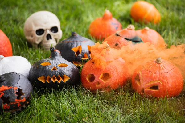 Carved pumpkins with orange smoke near blurred skull on green lawn — Stock Photo