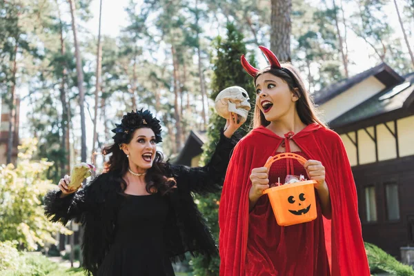 Woman in vampire halloween costume screaming and scaring daughter with skull and toy hand — Stock Photo