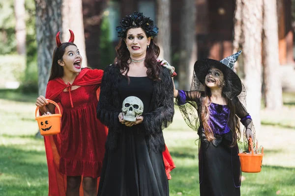 Chicas en diablo y bruja halloween trajes asustando a mamá asustada en el bosque - foto de stock