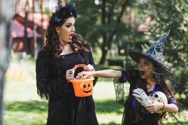 Woman in vampire halloween costume screaming while daughter stealing candies from bucket — Stock Photo