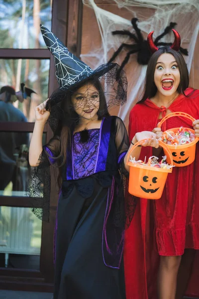 Excited and happy girls in halloween costumes, with buckets of candies on house porch — Stock Photo