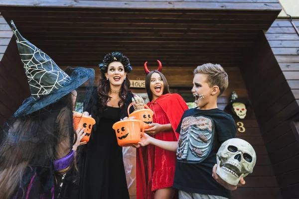 Vista de ángulo bajo de la familia emocionada en trajes espeluznantes de Halloween gritando en el porche de la casa - foto de stock