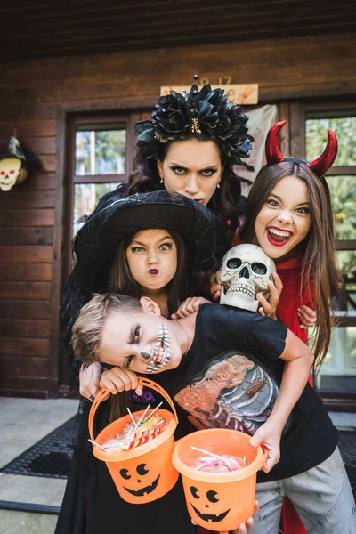 Família em trajes de Halloween, com crânio assustador e balde de doces sorrindo e rosnando para a câmera — Fotografia de Stock