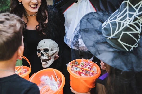 Family in halloween costumes, with skull and buckets with sweets — Stock Photo