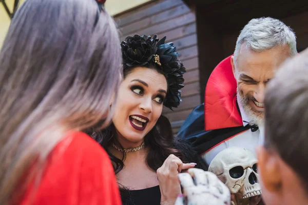 Frau im Halloween-Kostüm zeigt auf Totenkopf, während sie mit verschwommenen Kindern spricht — Stockfoto