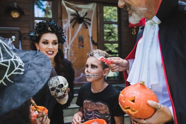 Чоловік тримає цукерки поблизу збудженої сім'ї в костюмах Хеллоуїна — стокове фото