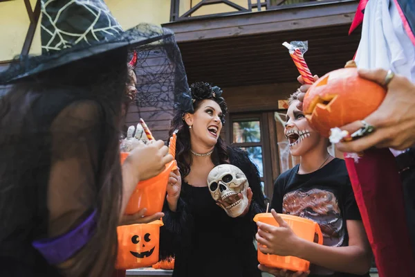 Familia emocionada en disfraces de Halloween gritando mientras sostiene cubos y dulces - foto de stock