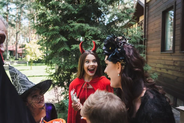 Eccitata ragazza in costume diavolo Halloween vicino alla famiglia all'aperto — Foto stock