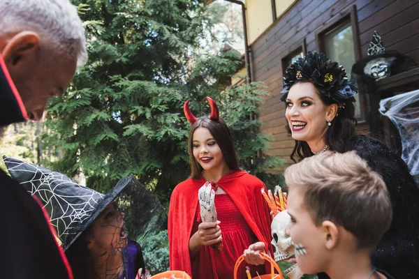 Весела дівчина тримає іграшкову руку біля сім'ї в моторошних костюмах Хеллоуїна — стокове фото