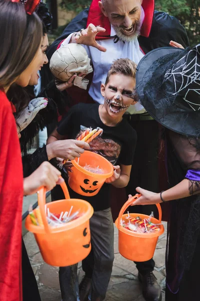 Family in halloween costumes grimacing while holding buckets with sweets — Stock Photo
