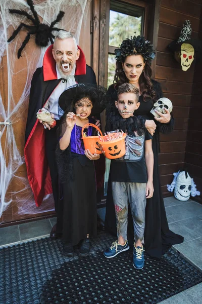 Famille effrayante en costumes d'Halloween grimacant sur le porche avec décoration — Photo de stock