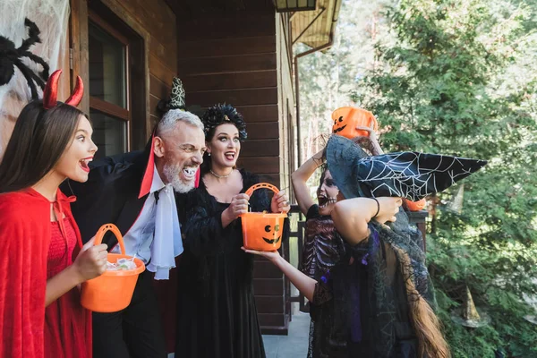 Excited couple in spooky halloween costumes scaring kids near house — Stock Photo