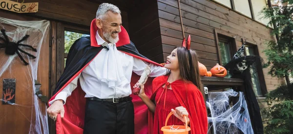 Felice papà e figlia in costumi di Halloween vicino portico con decorazione, banner — Foto stock