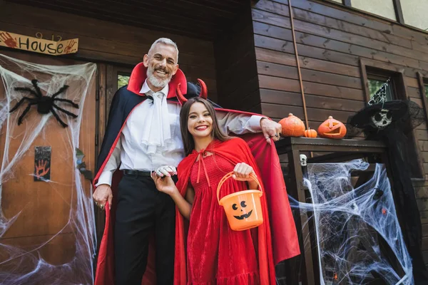 Glücklicher Vater und Tochter in Halloween-Kostümen nahe Hütte mit Dekoration — Stockfoto