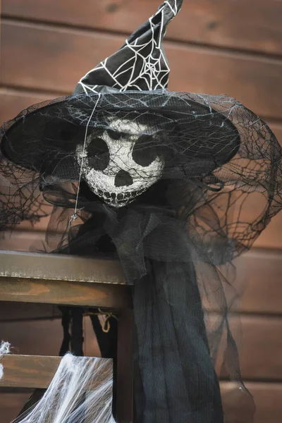 Scarecrow in witch hat with black veil on fence of wooden cottage — Stock Photo