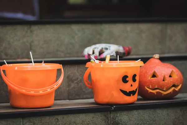 Halloween buckets with sweets near carved pumpkin and blurred toy hand on stairs — Stock Photo