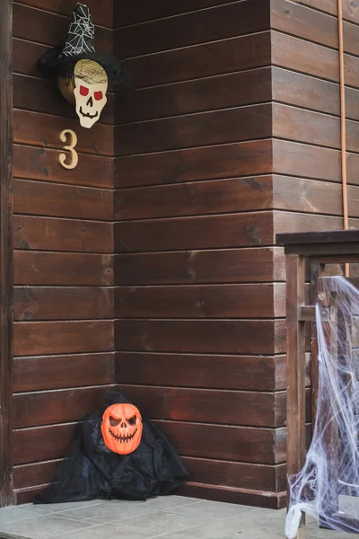 Porch of wooden cottage decorated with carved pumpkin, spider net and paper cut skull in witch hat — Stock Photo