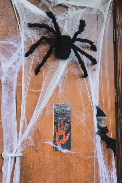 Puerta decorada con araña de juguete, murciélago de papel cortado y red de araña cerca de placa de muestra con que me mataron letras - foto de stock