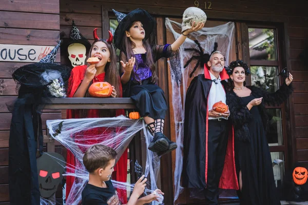 Familie in gruseligen Kostümen hat Spaß auf Hüttenveranda mit Halloween-Dekoration — Stockfoto