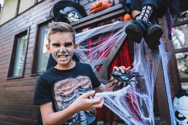 Mueca chico en esqueleto traje jugando con juguete araña cerca hermanas - foto de stock