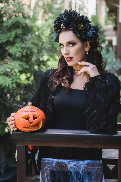 Frau in schwarzem Halloween-Kleid steht mit geschnitztem Kürbis auf Holzbalkon — Stockfoto
