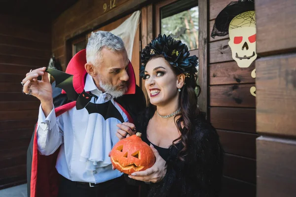 Woman with halloween pumpkin grimacing near husband with paper cut bat — Stock Photo