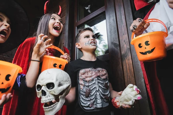 Spooky kids in halloween costumes shouting and growling at man with bucket — Stock Photo