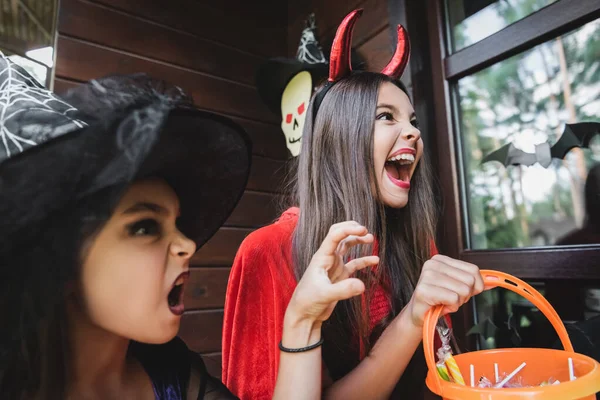 Spooky sisters in halloween costumes screaming and growling on cottage porch — Stock Photo