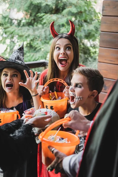 Kinder in gruseligen Halloween-Kostümen knurren verschwommene Nachbarn mit Bonbons an — Stockfoto