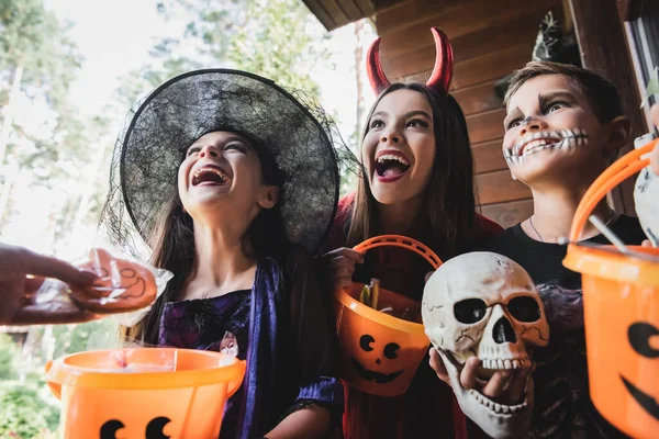 Enfants stupéfaits en costumes effrayants tenant des seaux près de maman avec biscuit halloween — Photo de stock