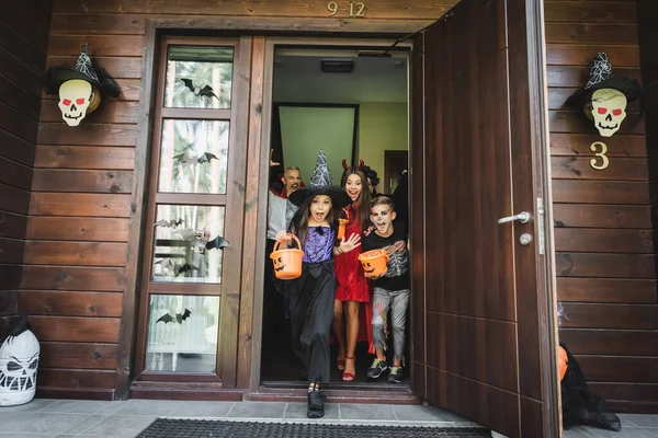 Діти в сумних костюмах, що виходять з сусідського будинку з прикрасою Хеллоуїна — стокове фото
