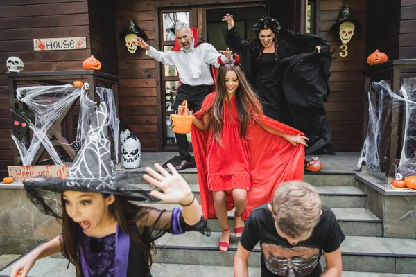 Emocionados niños con atributos de Halloween gritando mientras huyen de los vecinos - foto de stock